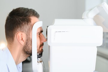 Handsome man getting an eye exam at ophthalmology clinic. Checking retina of a male eye