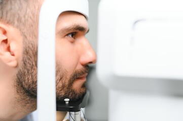 Handsome young man is checking the eye vision in modern ophthalmology clinic. Patient in...