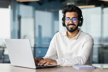 Portrait of Indian fashionable man businessman. a dancer working in the office on a laptop, wearing headphones, looks and smiles at the camera