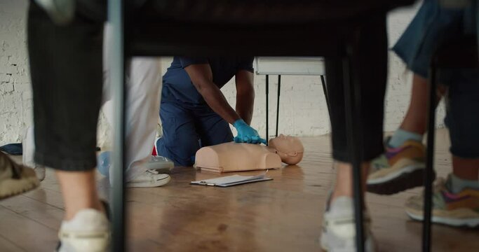 Bottom view: A Black male doctor in a blue uniform conducts a training practical training on artificial respiration together with his assistant in a white uniform