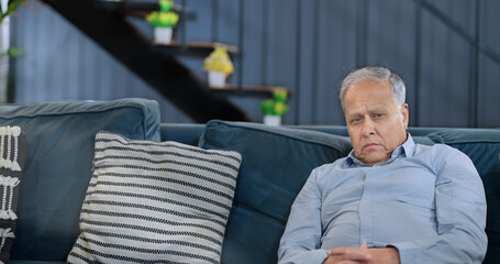 Worried retired Asian old senior man sitting alone sofa couch feel bad sorrow anxiety at indoor home. Indian elder aged Gray haired gen x male sad lonely pensive suffer ill health issues problem