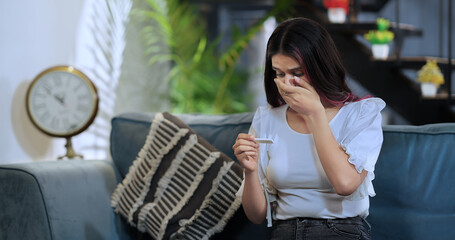 Asian Indian Hindu young adult fail sad woman lady wife sitting sofa couch hold kit check tester...