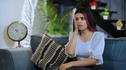 Indian tired tense abuse afraid young female girl sitting sofa couch watch bad TV news indoor house...