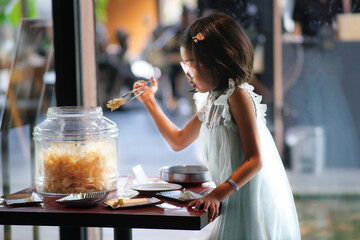 A little girl is taking some crackers from a glass container