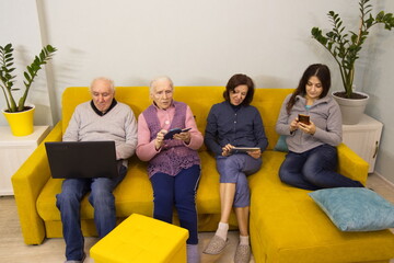 Family members use a laptop, tablet PC and smartphones. Grandfather, grandmother, middle-aged woman...
