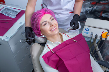 Closeup of female patient showing her beautiful white teeth while having treatment at dental clinic, dentist hands in rubber gloves holding dental tools