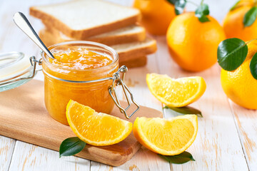 Obraz na płótnie Canvas Jar of tasty orange jam on a white wooden table. Slices of bread with orange jam for breakfast .
