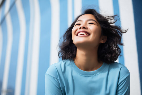 photo of a smiling asian woman in blue casualwear sweater in front of a striped tent background