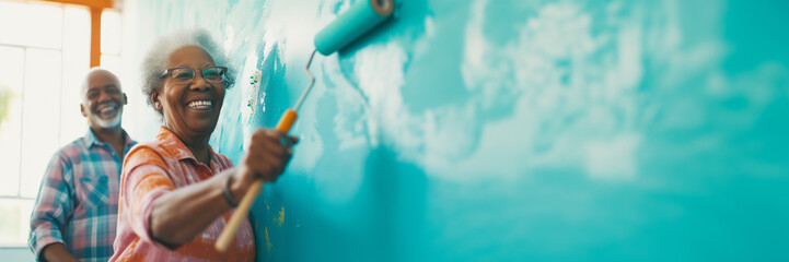 A joyful African American senior woman is painting a wall turquoise, with an African American man smiling in the background - Powered by Adobe