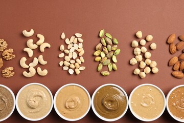 Many tasty nut butters in bowls and nuts on brown table, flat lay