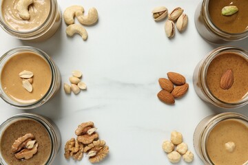 Tasty nut butters in jars and raw nuts on white marble table, flat lay
