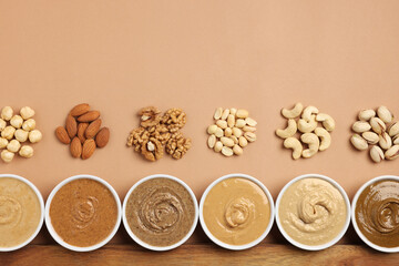 Many tasty nut butters in bowls and nuts on beige table, flat lay. Space for text