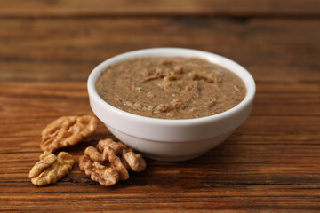 Delicious nut butter in bowl and walnuts on wooden table, closeup