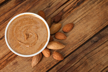 Delicious nut butter in bowl and almonds on wooden table, top view. Space for text
