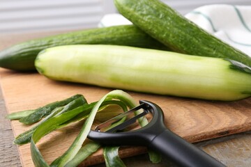 Fresh cucumbers, peels and peeler on wooden table, closeup