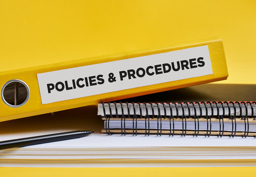 Policies and procedures written on the label of a yellow binder on the office desk
