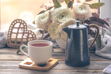Cozy home composition with a cup of tea, teapot and flowers.