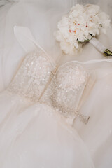 A modern wedding dress lies on a stylish chair in the soft morning light. Stylish wedding dress with sparkles shimmering in the light.