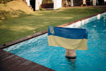 a young man abroad rests in the pool with a patriotic towel in the form of the Ukrainian flag