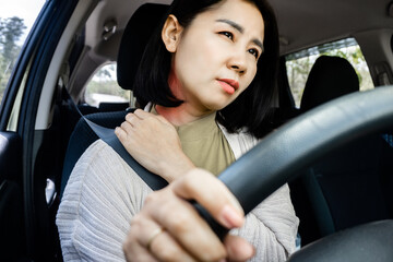 Asian woman suffering from neck and shoulder pain while driving sitting behind the wheel of car , hand holding muscle pain