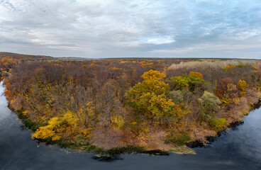 Aerial panorama autumn river with blue mirror water, yellow forest landscape and cloudy sky. Wild riverside nature in Ukraine