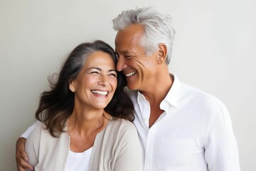 Elderly loving couple standing close together and smiling leaning against a white wall. AI generated