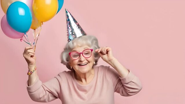 Cheerful grandmother with balloons celebrating birthday party. Happy grandma old woman wearing party hat on pink pastel background