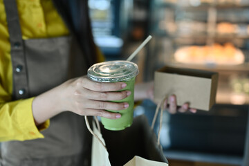 Waitress putting coffee plastic cup into paper bag at counter in cafe. Food delivery and takeaway food concept