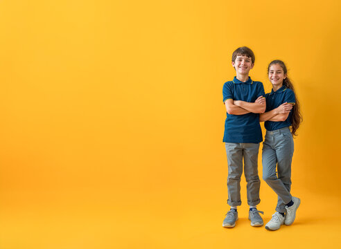 deux &eacute;coliers en uniforme scolaire, polo bleu et pantalon gris - fond jaune
