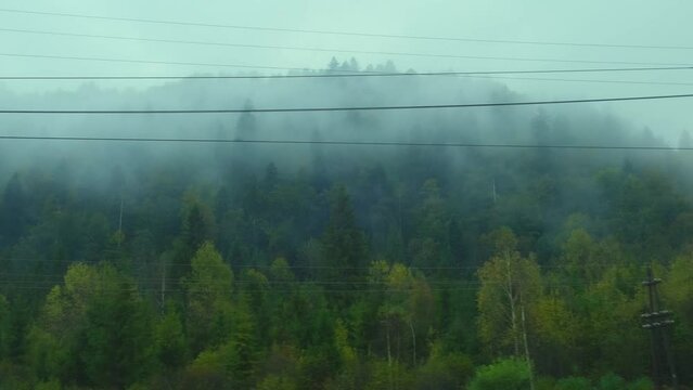 Mountains view through train window. Passenger train compartment passing by electric wires. Mountain peaks in the morning fog. Traveling by train, nature of Ukraine