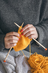 A woman's hands with red nails are knitted from yellow yarn.