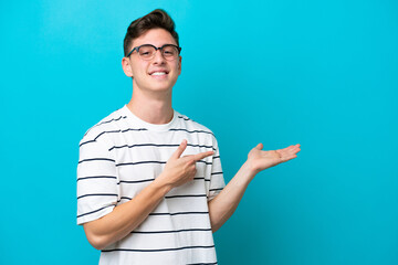 Young handsome Brazilian man isolated on blue background holding copyspace imaginary on the palm to...