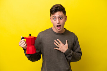 Young Brazilian man holding coffee pot isolated on yellow background surprised and shocked while...