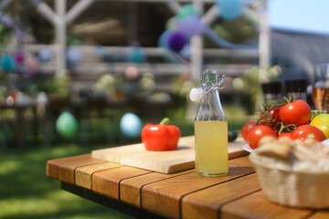 Close up shot of a grill and table at a summer garden party. Side table with wine glasses, lemonade, fresh vegetables, bread.