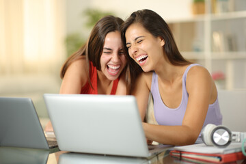 Happy students laughing watching media on laptop