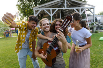 Handsome man playing at guitar for dancing friends at party. Friends and family dancing and having fun at summer grill garden party.