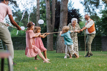 Grandparents have a tug of war with their grandkids. Fun games at family garden party. - obrazy, fototapety, plakaty