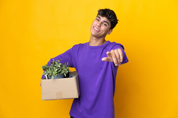 Man making a move while picking up a box full of things pointing front with happy expression