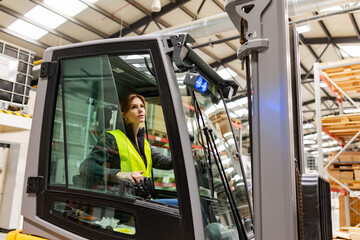 Fototapeta na wymiar Female warehouse worker driving forklift. Warehouse worker preparing products for shipmennt, delivery, checking stock in warehouse.