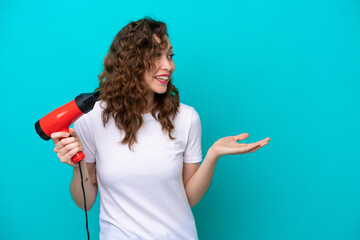 Young caucasian woman holding a hairdryer isolated on blue background with surprise facial...