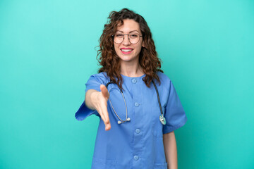 Young nurse caucasian woman isolated on blue background shaking hands for closing a good deal