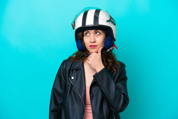 Young caucasian woman with a motorcycle helmet isolated on blue background having doubts