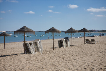 Set of umbrellas and hammocks, collected piled on top of each other on the beach by the end of the summer season with the sea in the background. Concept season, summer, end, change of season.