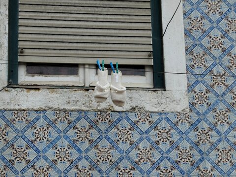 H&auml;ngende Sandalen in Lissabon - White sandals hanging from a shuttered window on a traditional azulejo-tiled fa&ccedil;ade in Lisbon, Portugal