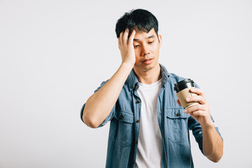 An exhausted Asian man, unable to wake up, stands holding a coffee cup. Studio portrait isolated on white, his tired expression speaks volumes. Copyspace available.