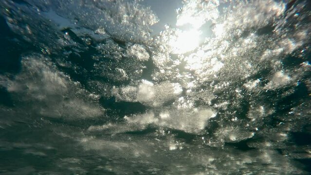 Movement of melting spring ice down the river in sun's rays at sunset, Underwater view, Slow motion. Evening sun light penetrates the underwater during ice drift.