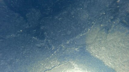 Underwater view of Ice drift, thin ice with air bubbles frozen into it quickly moves downstream on bright sunny day. Thin spring ice on blue sky background - Powered by Adobe