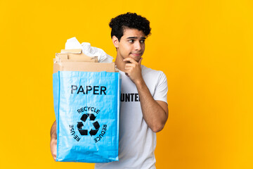 Young Venezuelan man holding a recycling bag full of paper to recycle having doubts and thinking