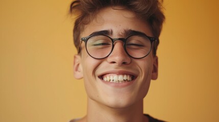 Young man with glasses smiling against a yellow background.