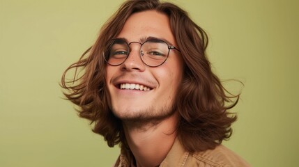 Fototapeta na wymiar Young man with long hair and glasses smiling against a green background.
